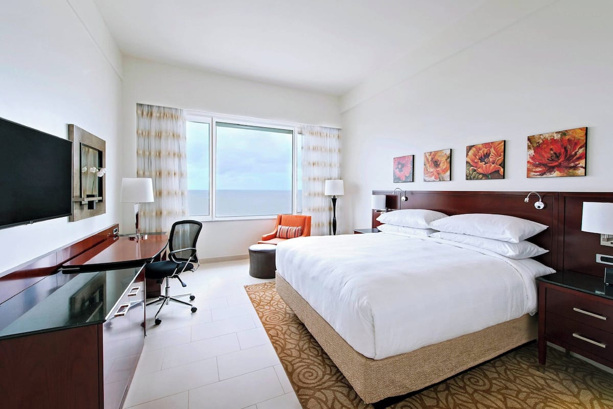A hotel room with a large bed, a desk with a chair, a television, and a window with curtains.