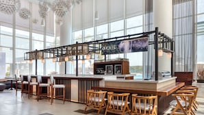 A modern bar area with a wooden bar counter, multiple stools, and a large window providing a view of the outdoors.