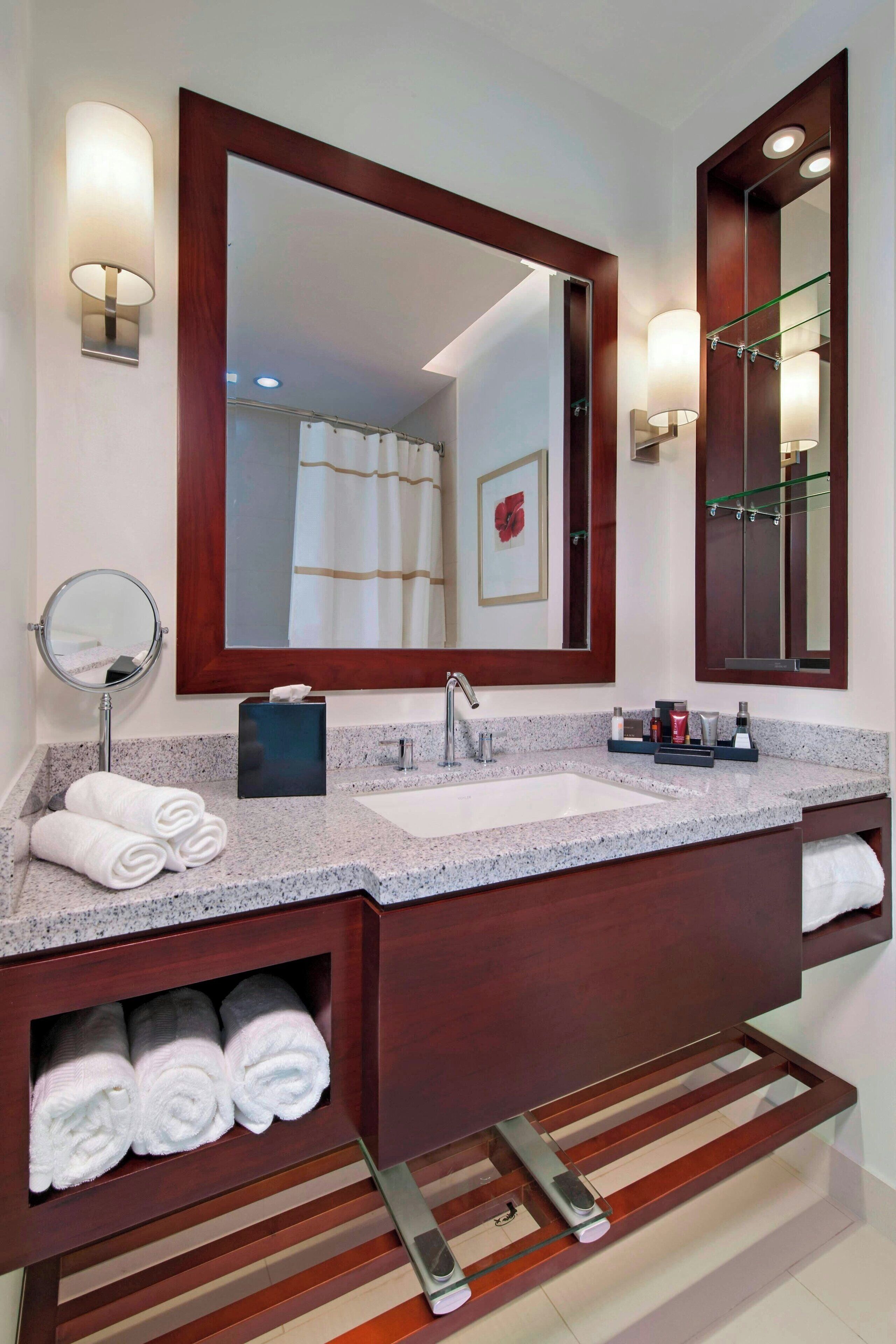 A modern bathroom with a granite countertop, a sink, a large mirror, and a towel rack.