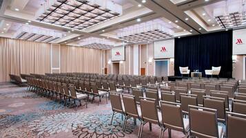 A conference room with rows of chairs, a stage, and a carpeted floor.