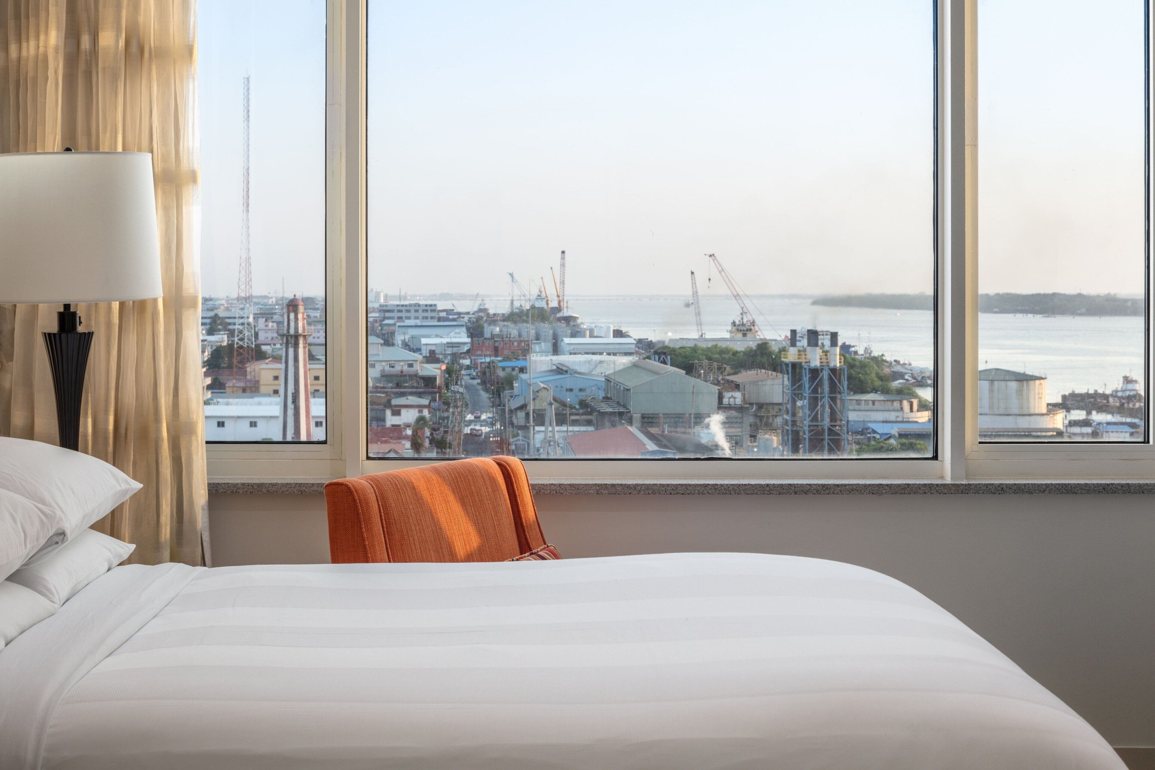 Habitación de hotel con una cama grande, una silla y vistas a la ciudad y al agua.