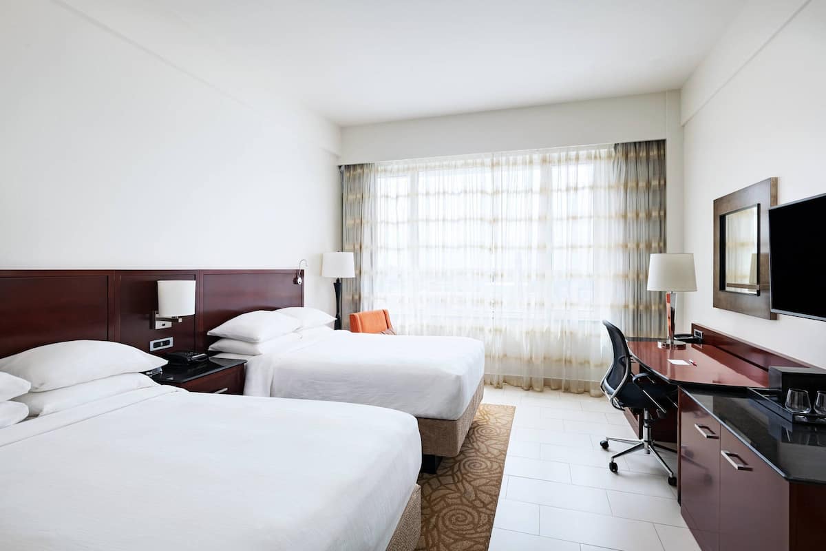 A hotel room with two beds, a desk, a chair, a TV, and a window with curtains.