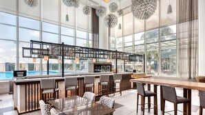 A modern bar area with a pool view, featuring a long counter, bar stools, and a dining table with chairs.