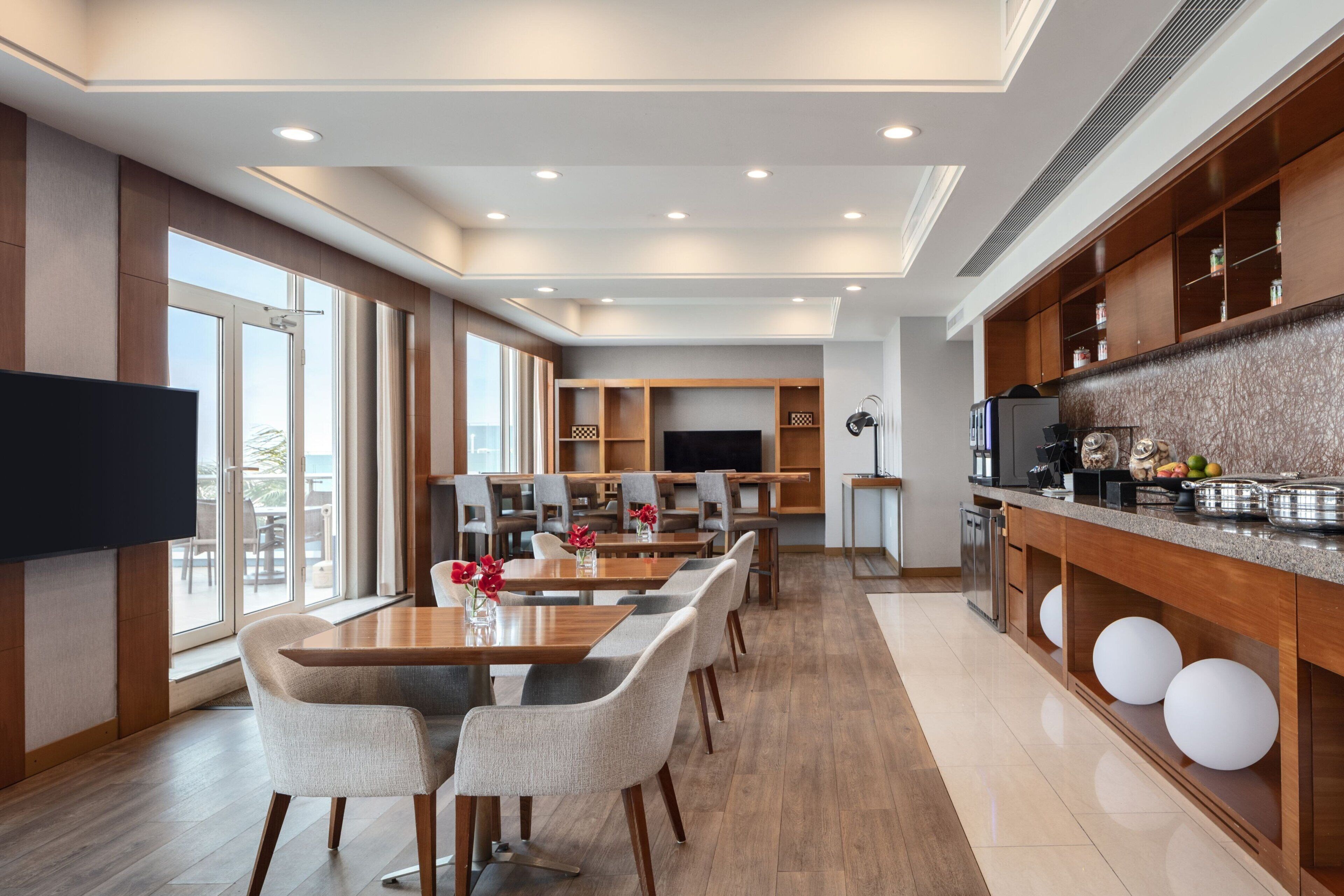 A modern hotel dining area with a long table, multiple chairs, and a television.