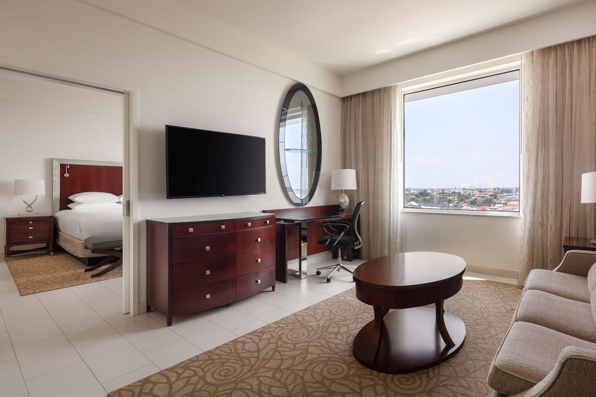 A hotel room with a bed, a desk, a TV, a large window, and a view of the city.