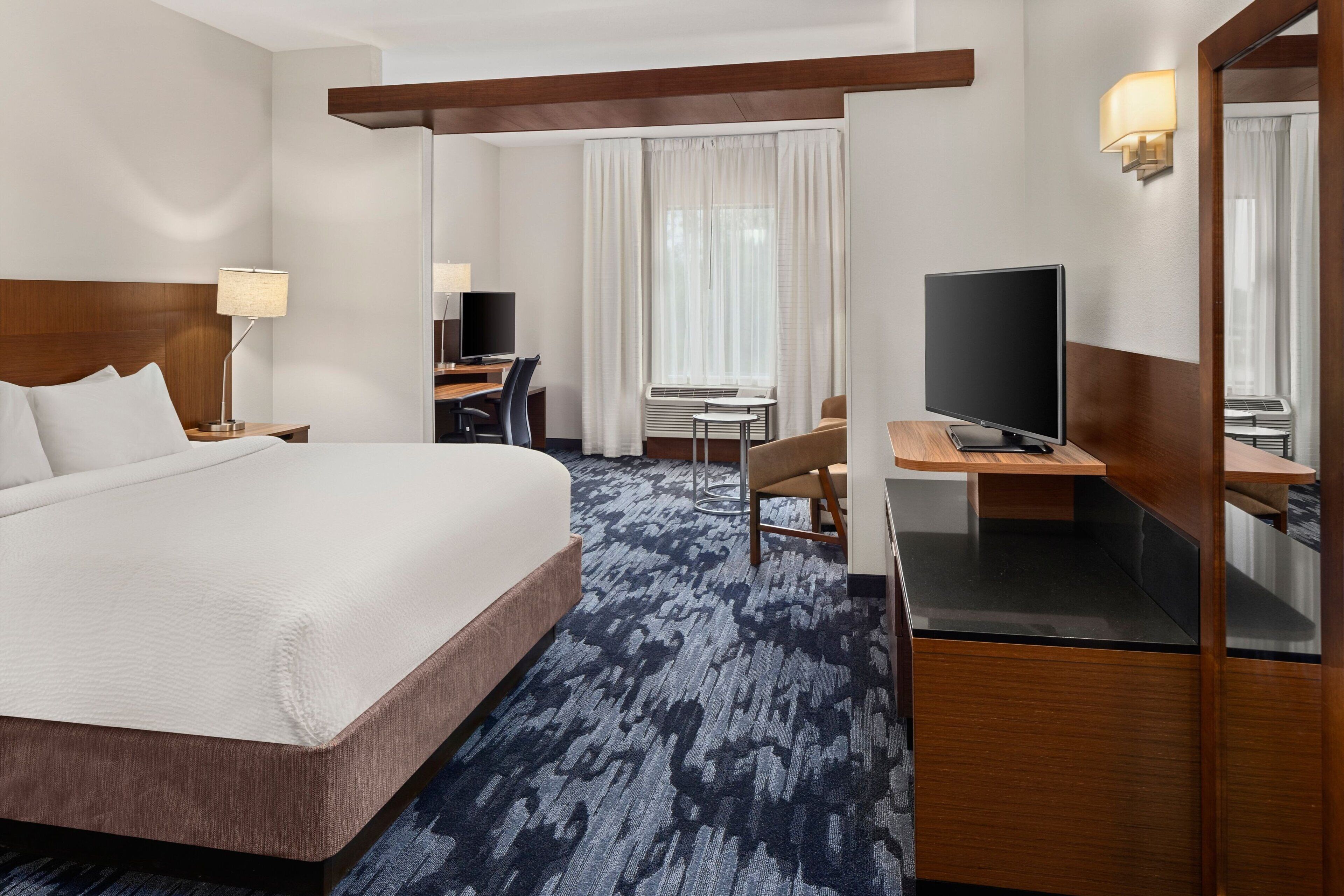 A hotel room with a large bed, a desk with a computer, a TV, and a mirror.
