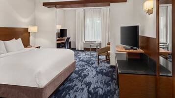 A hotel room with a large bed, a desk with a computer, a TV, and a mirror.