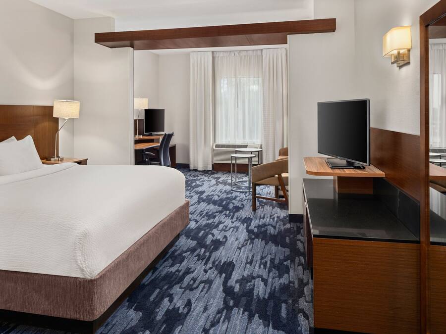 Una habitación de hotel con una cama grande, un escritorio con una computadora, un televisor y un espejo.