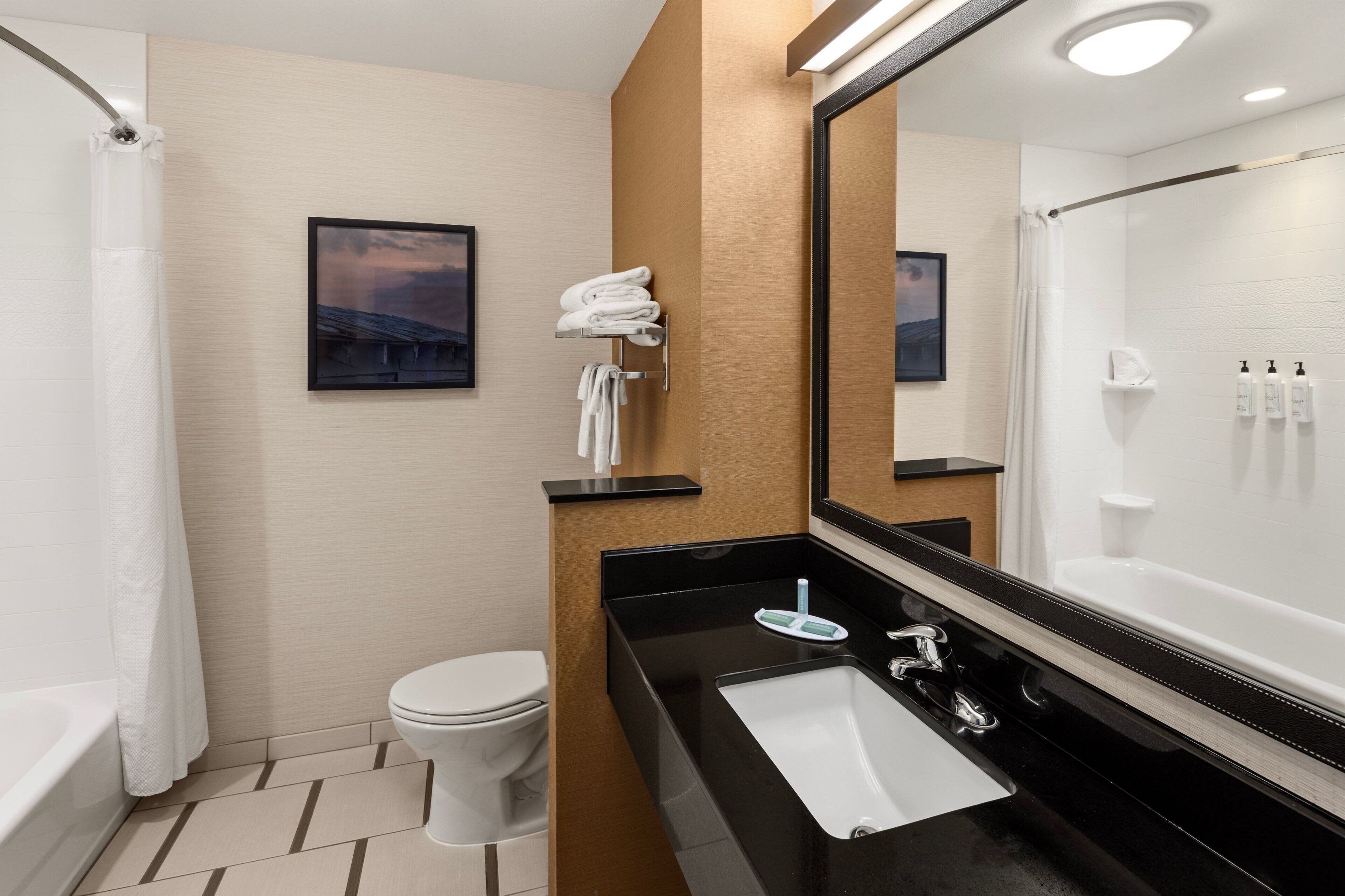 A modern bathroom with a bathtub, toilet, and sink. There is a towel rack with towels, a mirror, and a shower curtain.