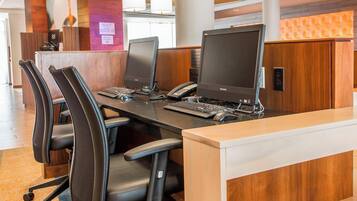 Uma sala de conferências com três cadeiras de escritório pretas, dois computadores de mesa, um telefone e um teclado.