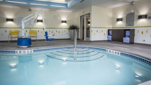 An indoor swimming pool with clear water, a lifeguard stand, and a changing room with towels.