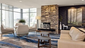 A modern living room with a stone fireplace, large windows, and a blue patterned rug.