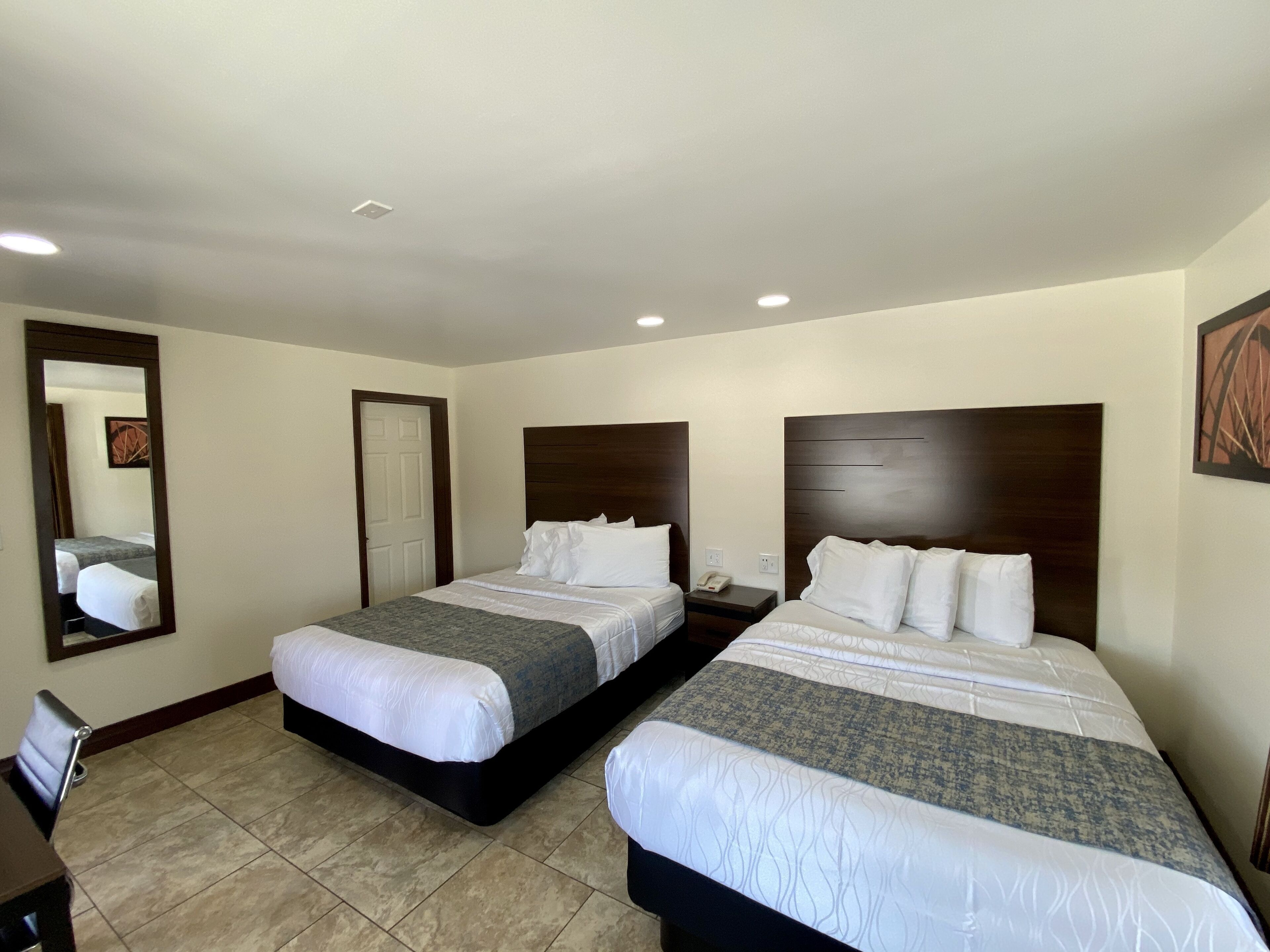 A hotel room with two beds, a large mirror, a bedside table with a phone, and a door.