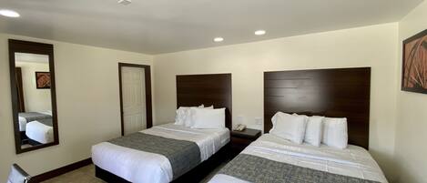 A hotel room with two beds, a large mirror, a bedside table with a phone, and a door.