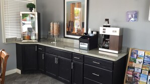A kitchen with dark cabinets, a coffee machine, and a window with blinds. - Roswell Inn (Roswell)