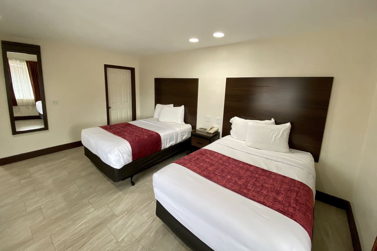 A hotel room with two beds, a nightstand, a mirror, and a door.