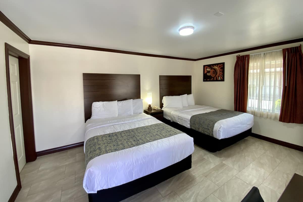 A hotel room with two beds, a ceiling light, a nightstand, a painting, and a window with curtains.