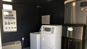 A laundry room with a wall-mounted sign listing soap, bleach, and softeners. There are two white appliances, one appears to be a washer and dryer, and the other a refrigerator. - Roswell Inn (Roswell)