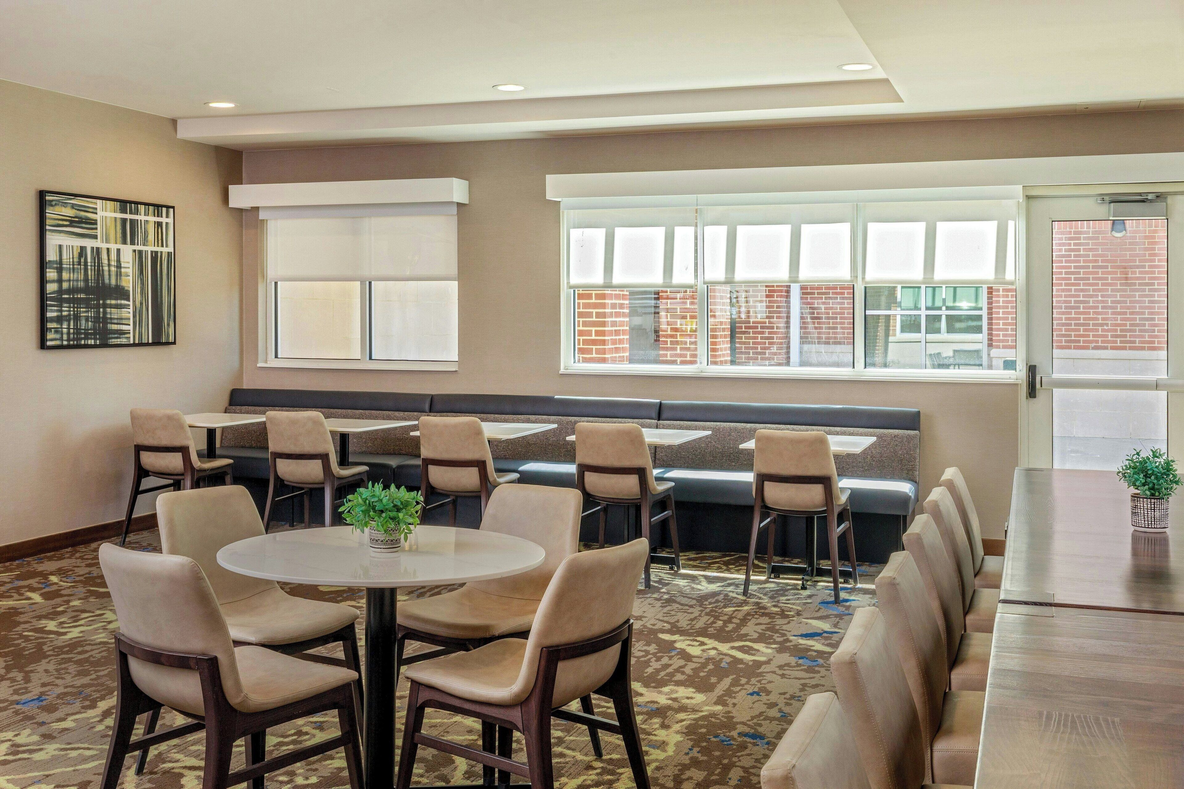 A conference room with a long table, several chairs, a sofa, and a window with a view of a brick building.
