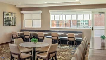 A conference room with a long table, several chairs, a sofa, and a window with a view of a brick building.