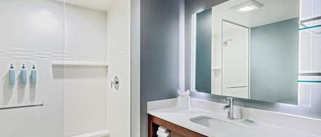 A modern bathroom with a large mirror, white tiles, and a glass shower enclosure.