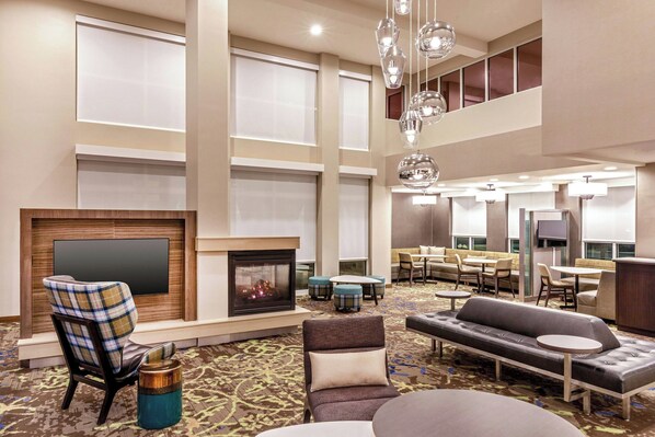 A spacious lobby with a fireplace, seating areas, and a high ceiling with hanging lights.