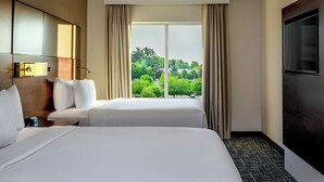 A hotel room with two beds, a large window with curtains, a flat-screen TV, and a wooden headboard.