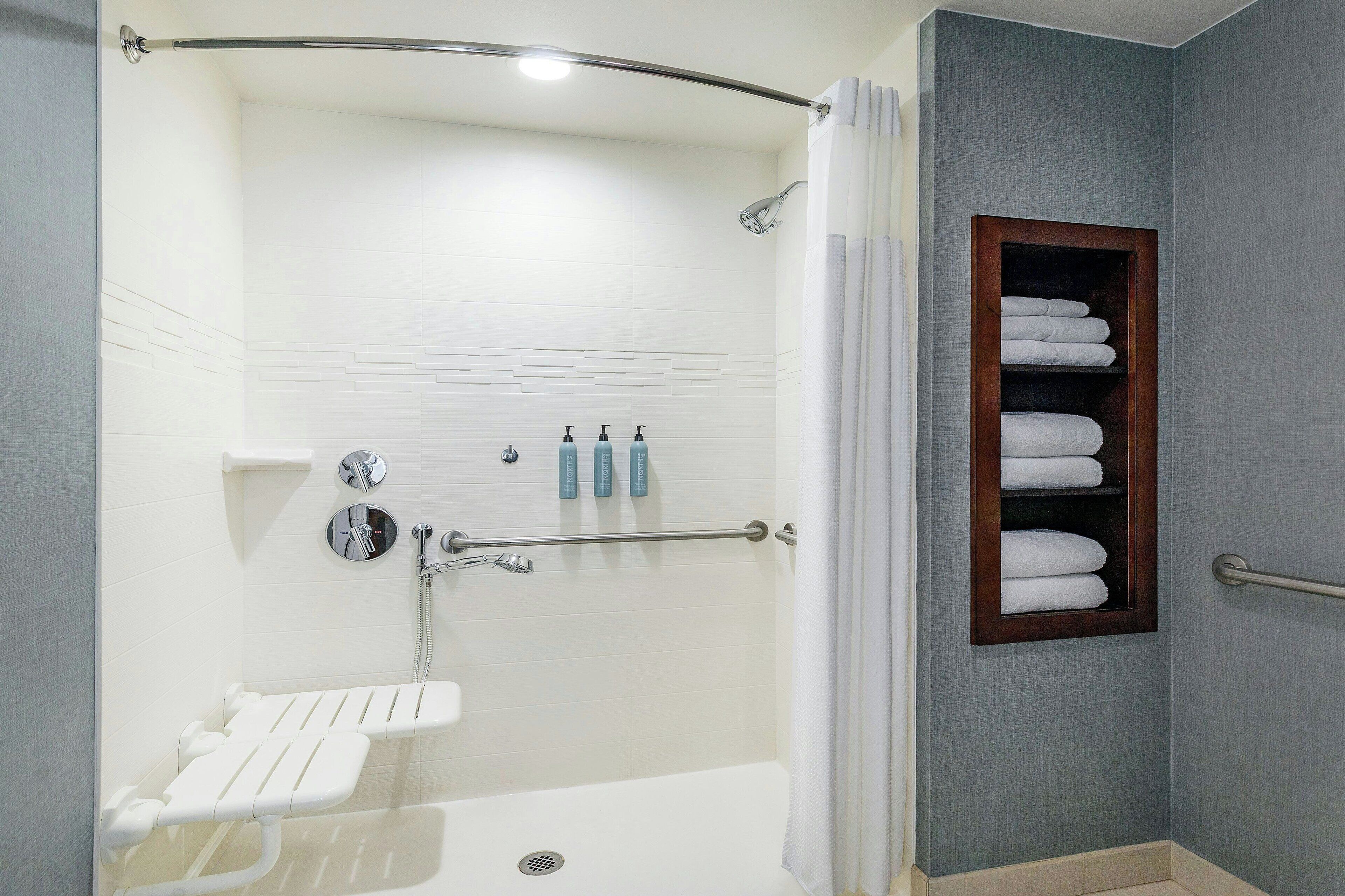 Un baño moderno con cabina de ducha, toallero empotrado y un lavamanos pequeño.