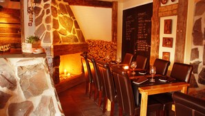 Ein Restaurant mit Steinsäulen, einem Kamin, Holztischen und Ledersesseln.