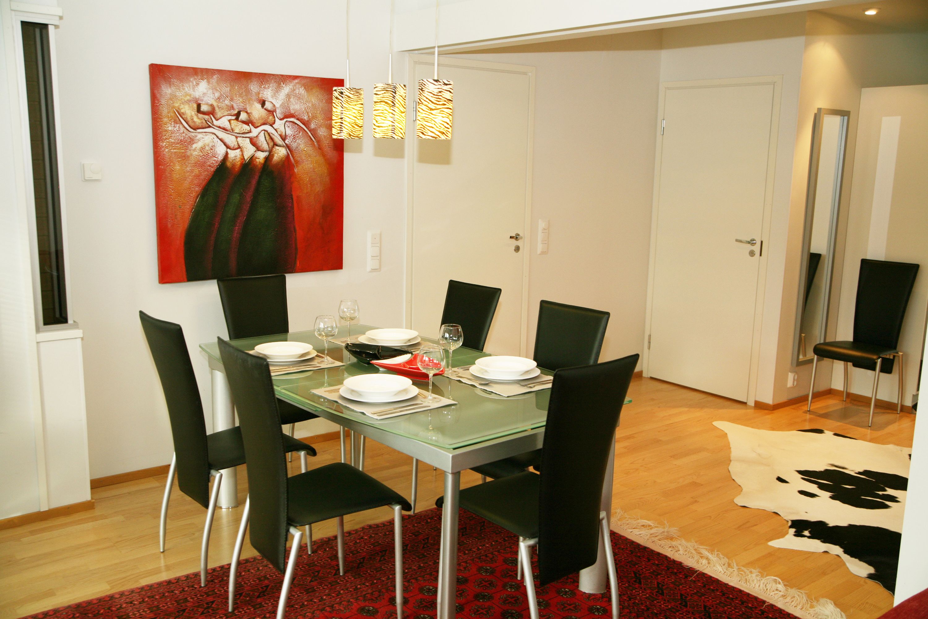 Un coin repas avec une table en verre, des chaises noires et un tapis rouge à motifs.