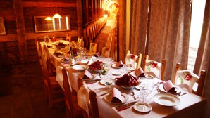 Ein Esszimmer aus Holz mit einem langen Tisch, gedeckt für eine Mahlzeit, mit Stühlen mit floralen Verzierungen und einer Treppe im Hintergrund.