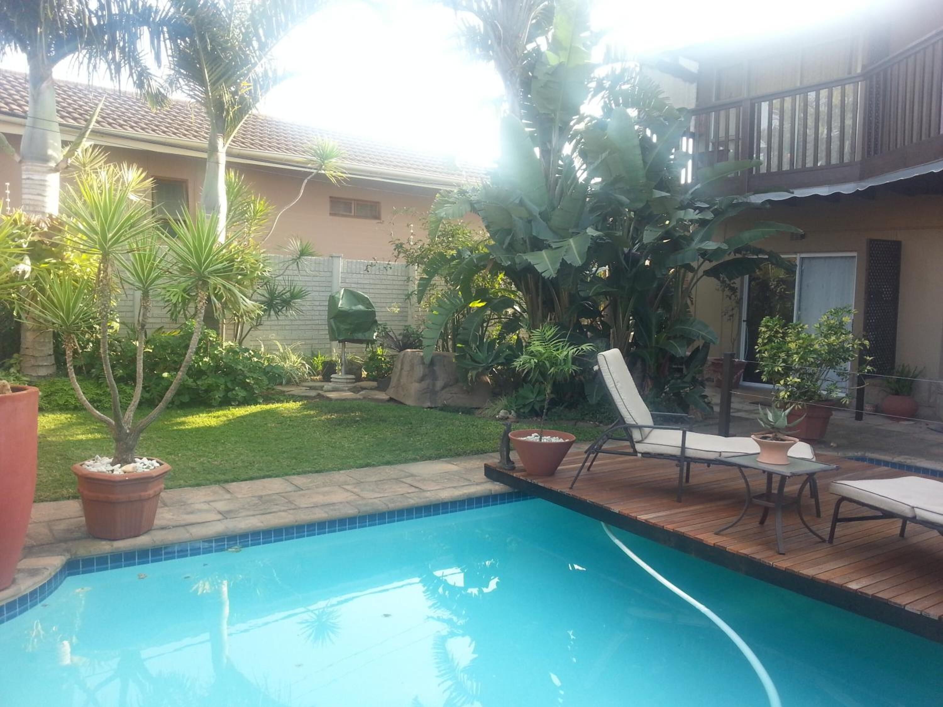 A backyard with a swimming pool, a wooden deck, and various potted plants.