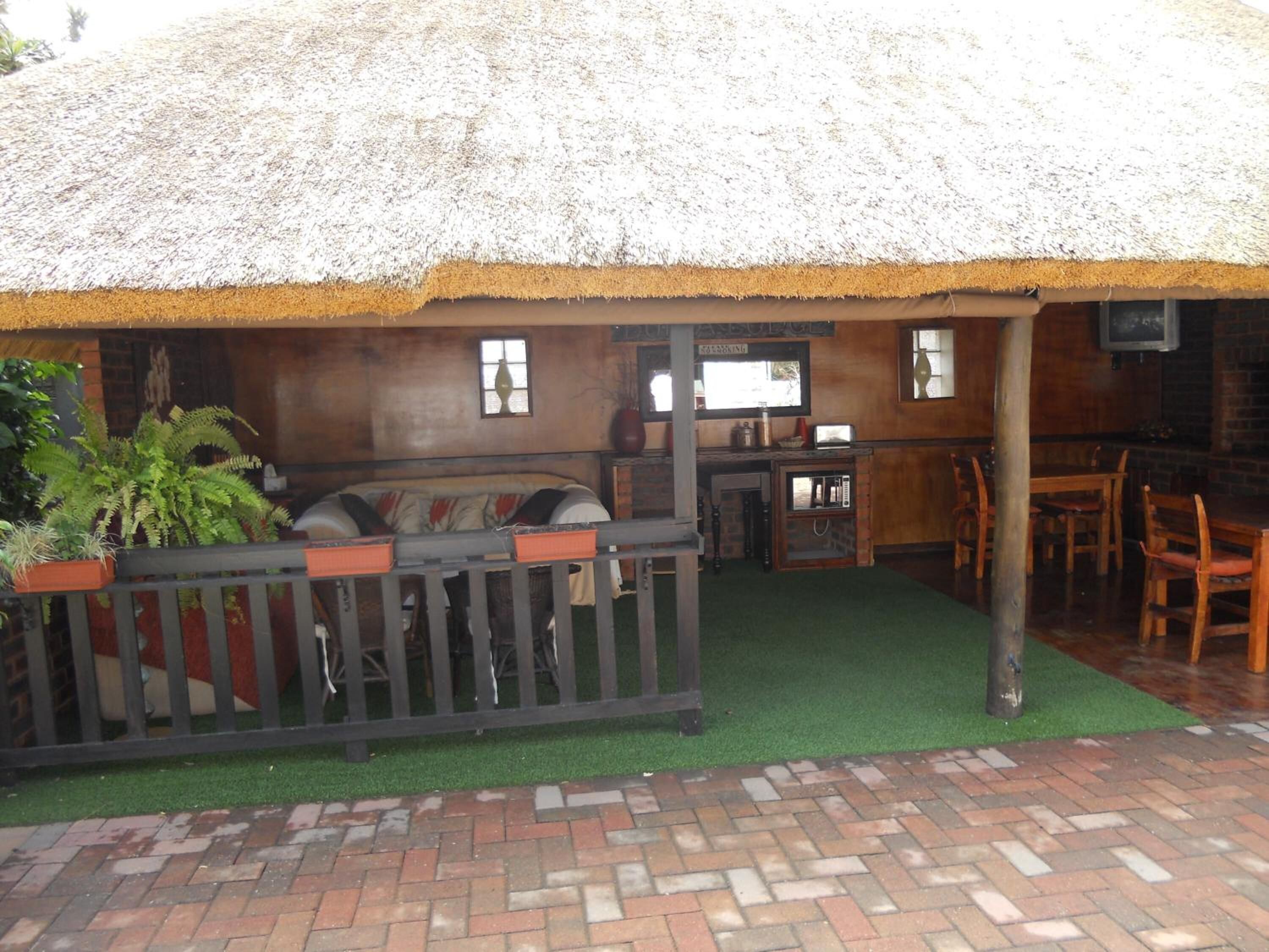 A rustic outdoor seating area with a thatched roof, a wooden table, and a brick floor.