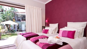 A hotel room with two beds, a balcony with a table and chairs, and a view of a building with a balcony. - Boma Lodge (Durban North)