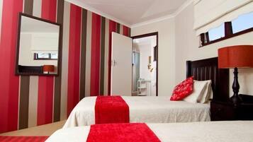 A hotel room with striped walls, two beds with red and white bedding, a wooden nightstand, a mirror, and a window with a view.