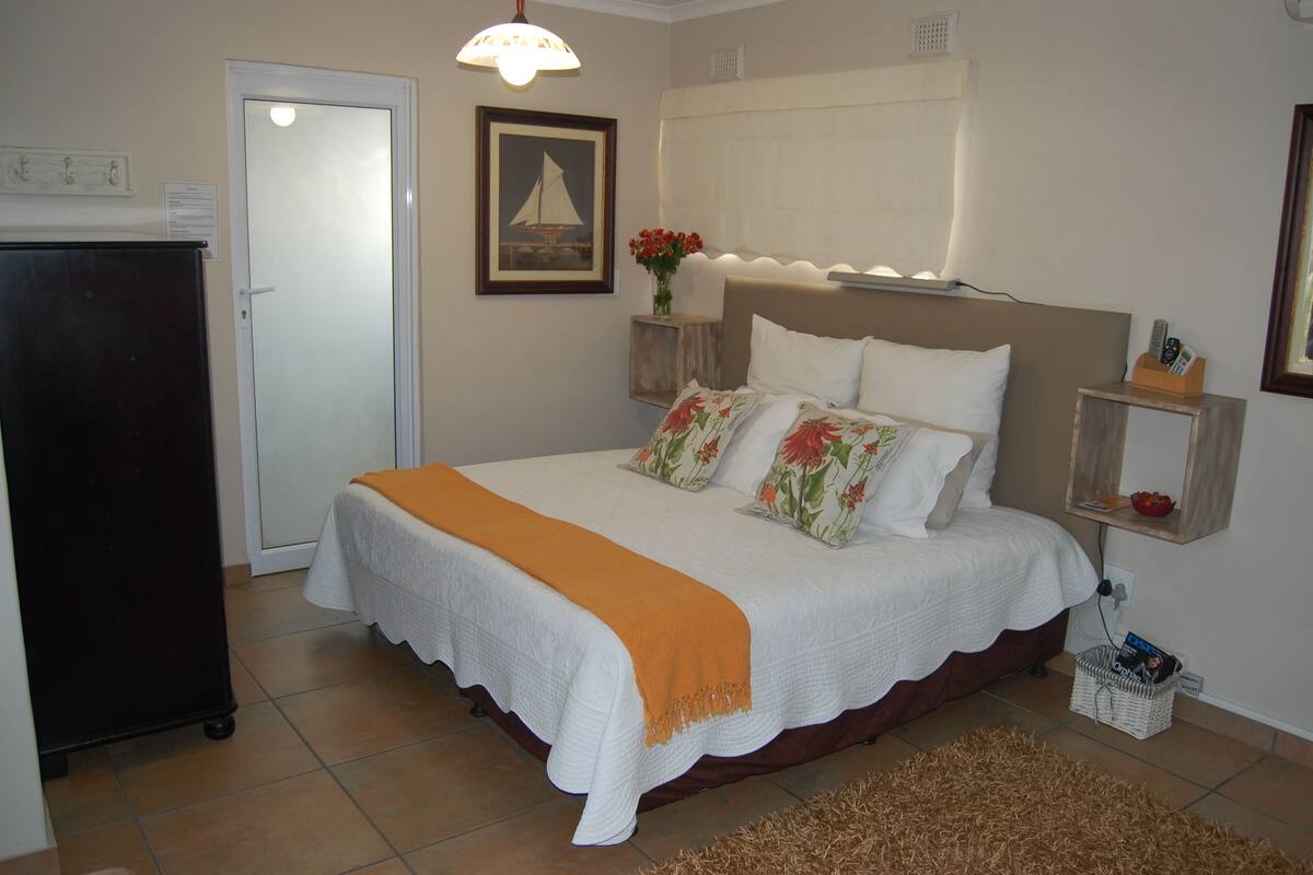 A neatly arranged bedroom with a bed, bedside tables, a dresser, and a door.
