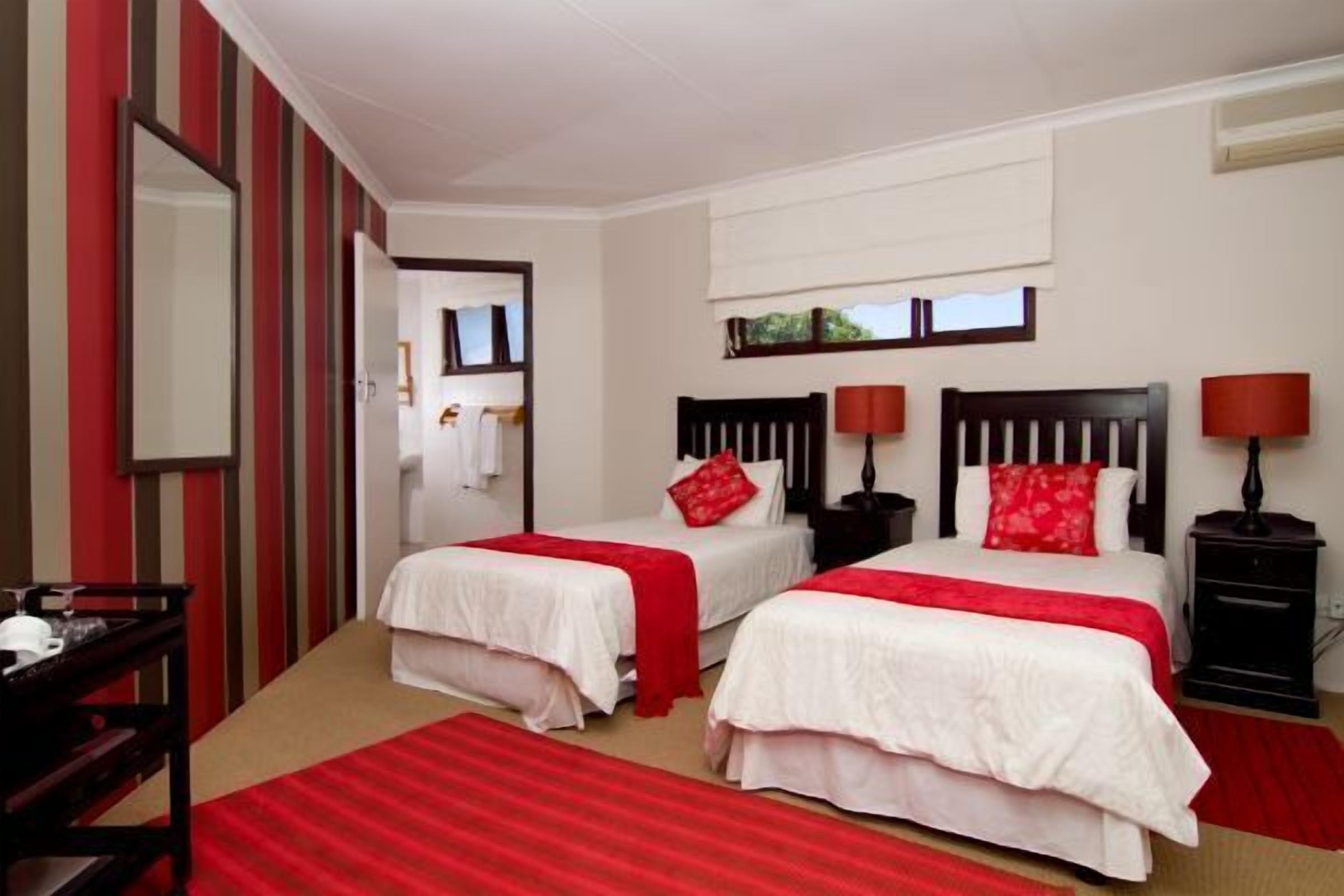 A hotel room with two beds, each with a red and white bedspread, a bedside table with a lamp, and a dresser.