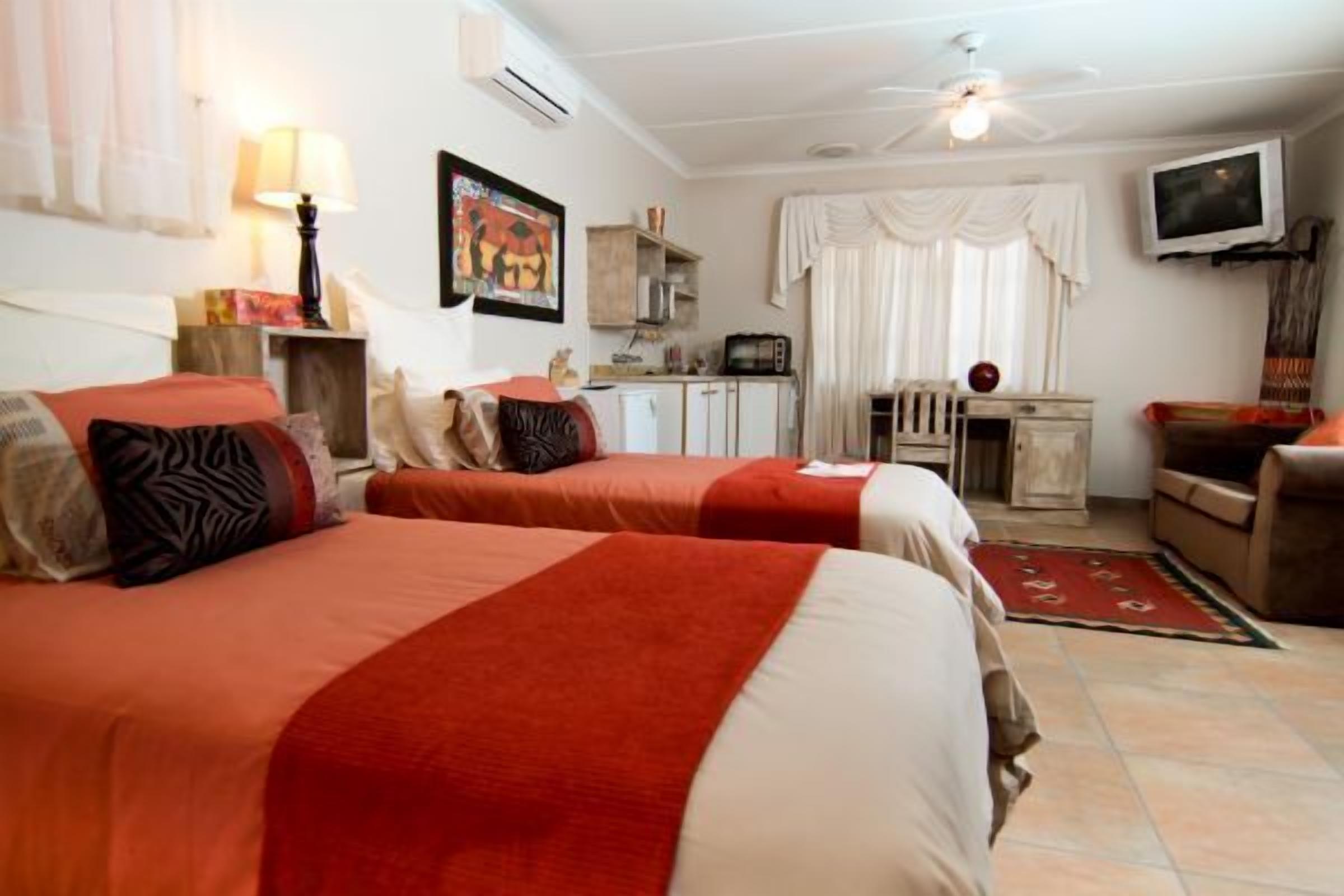 A hotel room with two beds, a kitchenette, a television, and a ceiling fan.