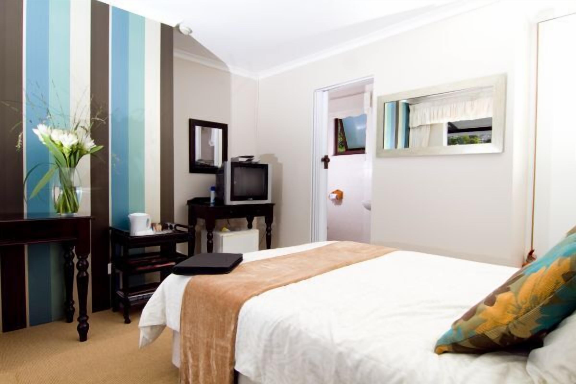 A hotel room with a bed, a desk with a computer, a television, and a vase with flowers.