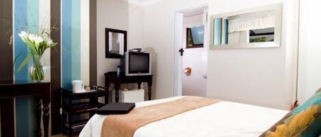 A hotel room with a bed, a desk with a computer, a television, and a vase with flowers.