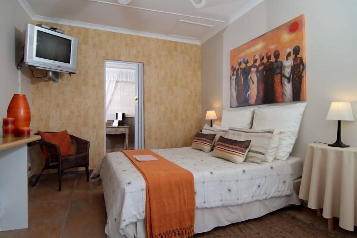A bedroom with a bed, a TV, a desk, a chair, and a painting on the wall.