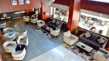 Relax in a spacious lounge with sofas, armchairs, and a coffee table, surrounded by a high ceiling and large windows.