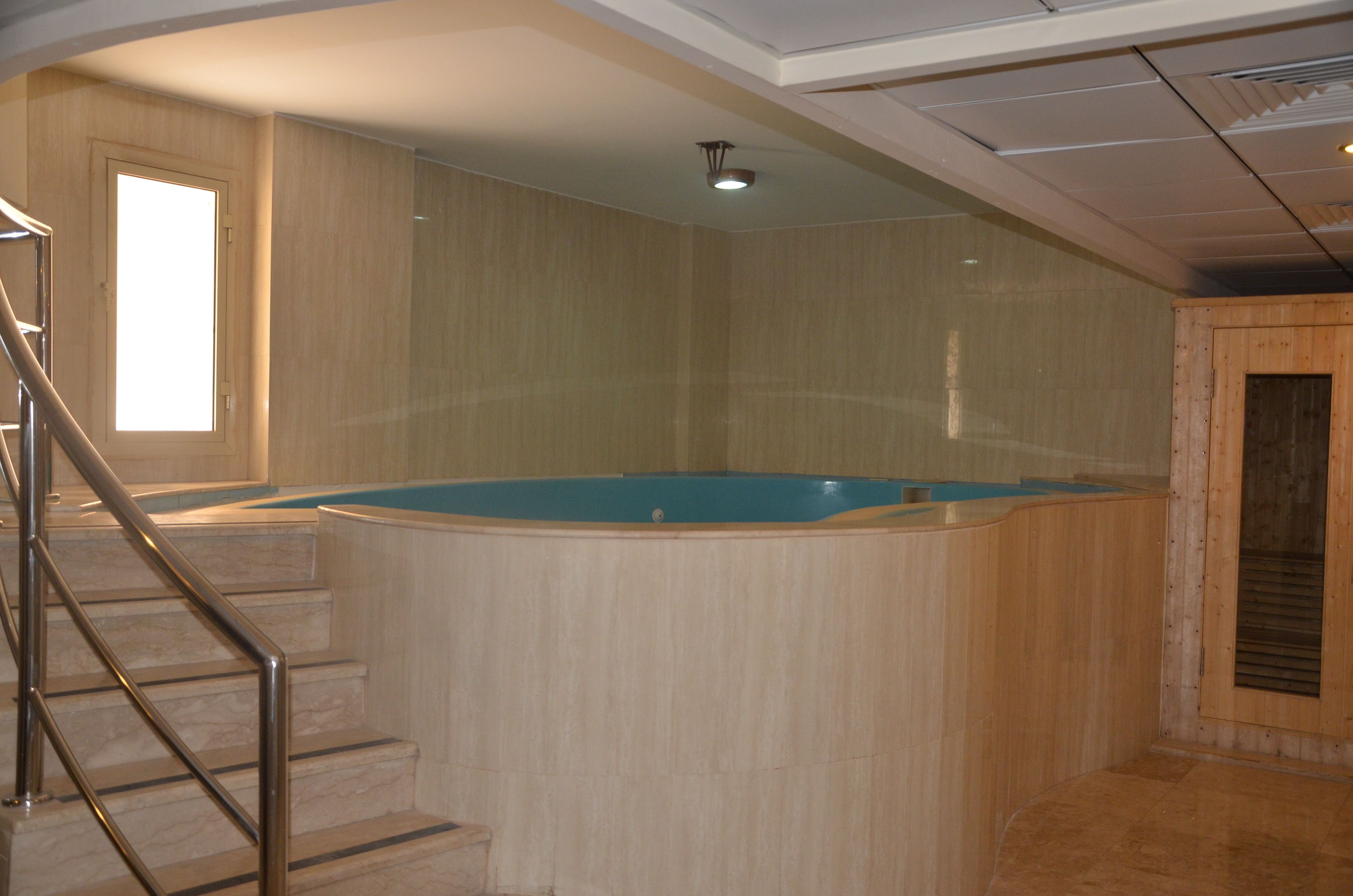 A room with a wooden spa tub, a staircase with metal railings, and a large window.