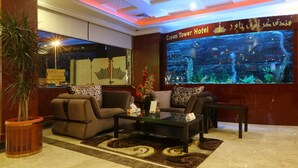 Et hotel lobby med en reception, to sofaer, et sofabord, et stort akvarium og en potteplante.