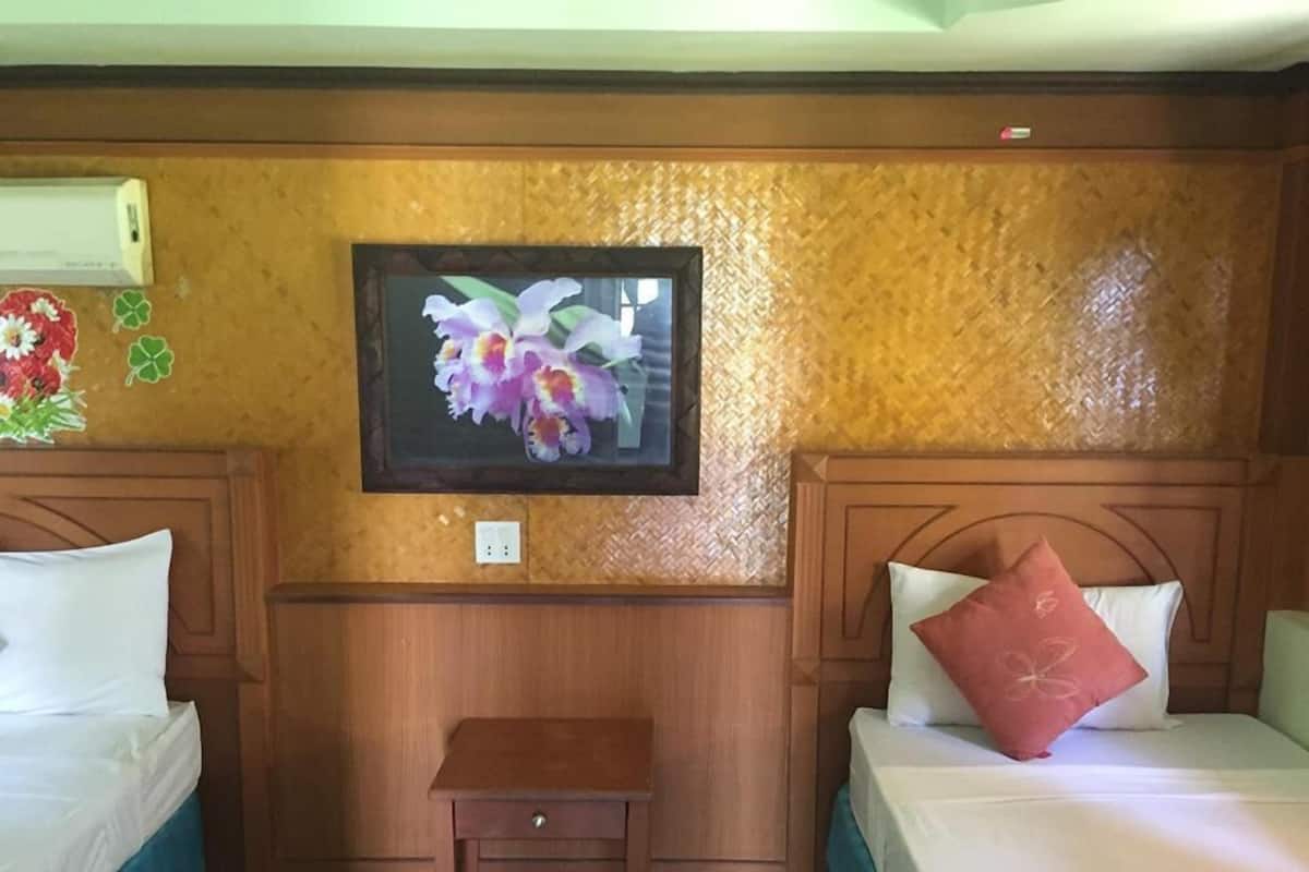 Quarto de hotel com duas camas, uma pequena mesa de cabeceira de madeira e uma obra de arte floral emoldurada na parede.
