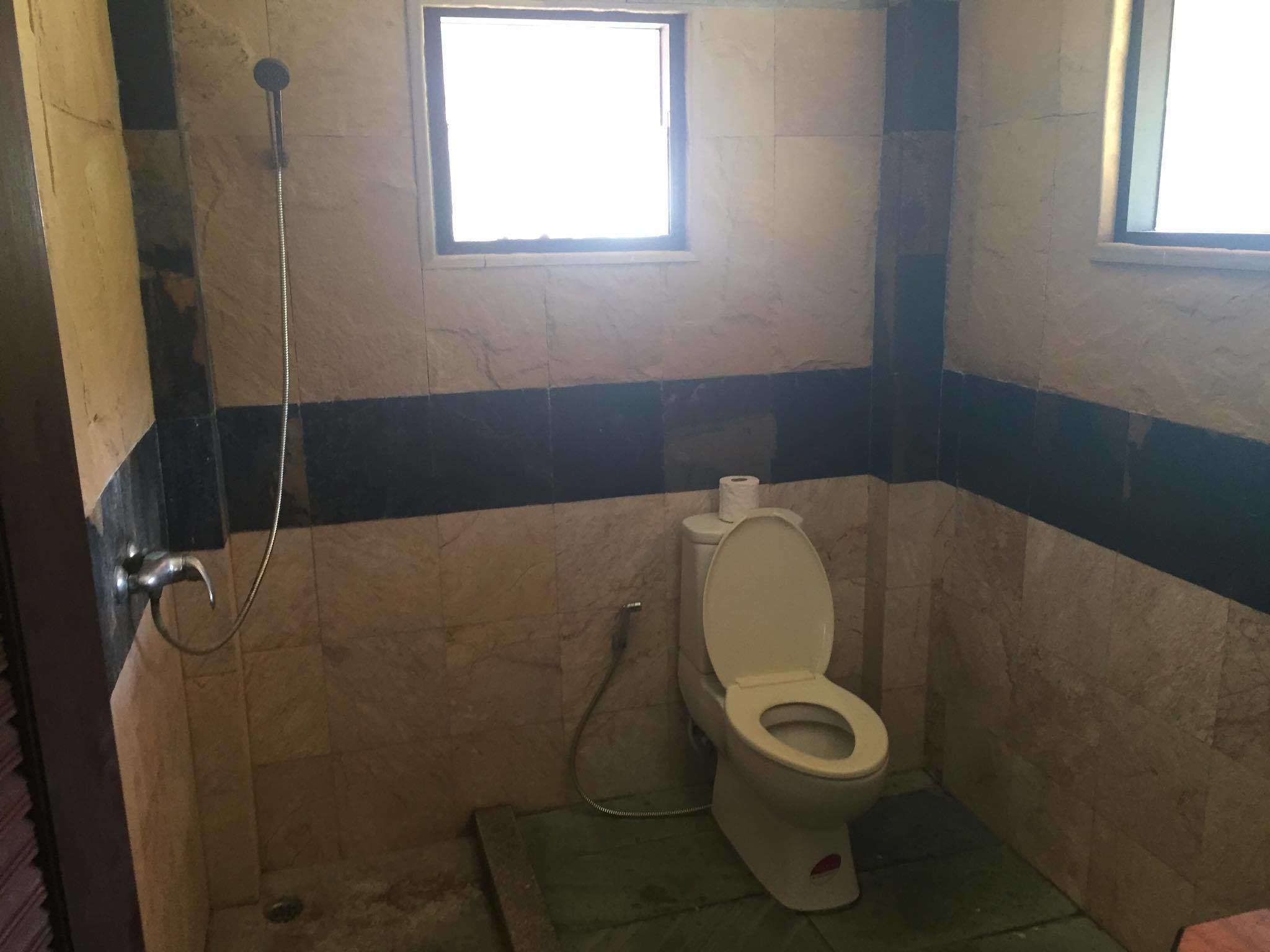 A small bathroom with a toilet, a shower, and a window.