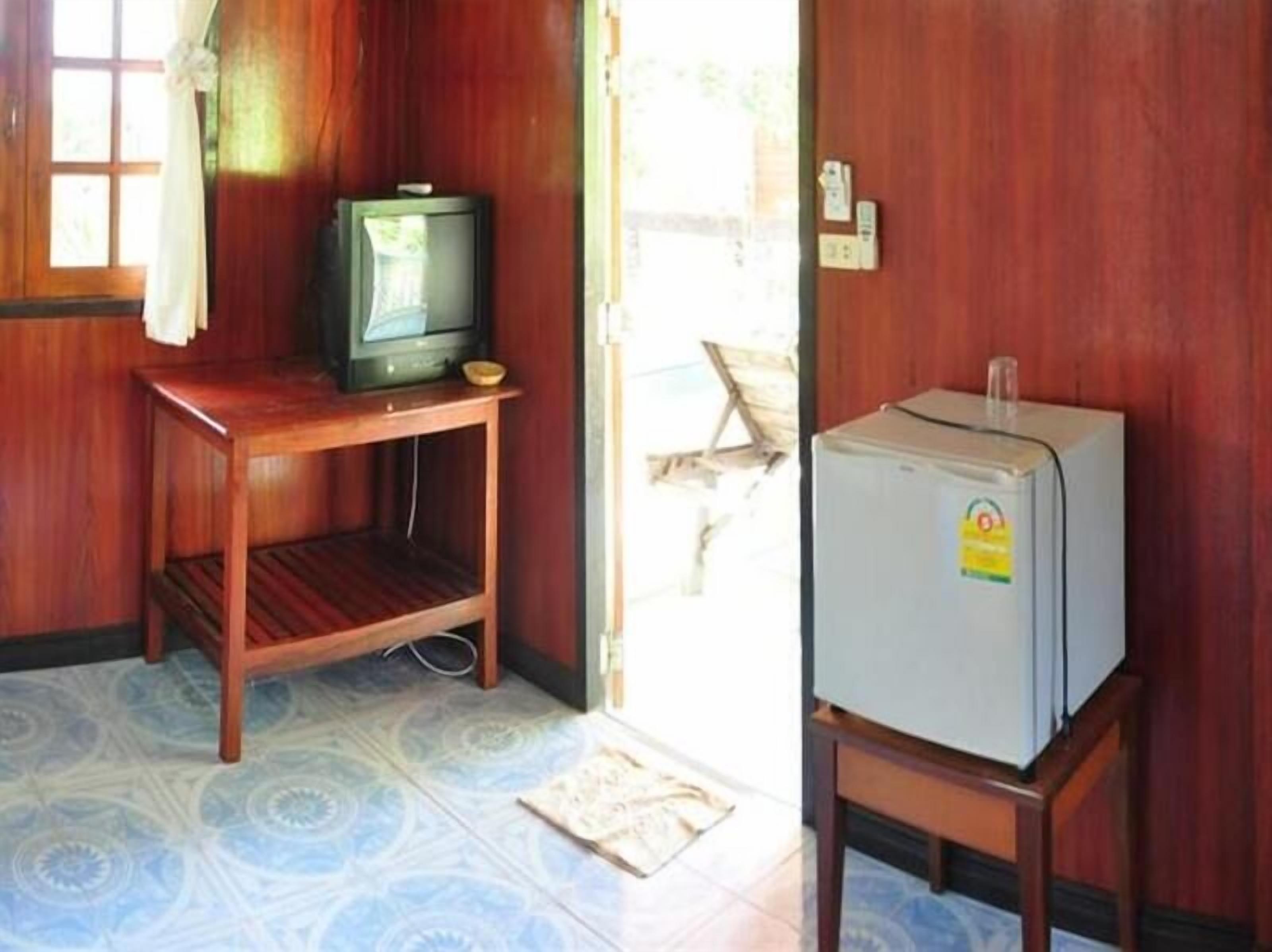 Una habitación con una mesa de madera, un televisor sobre un mueble bajo y un refrigerador en una mesita.