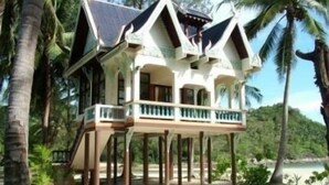 Une maison à deux étages avec un balcon, entourée de palmiers et donnant sur une plage.