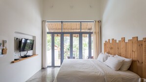 Un dormitorio con una cama, un televisor sobre una repisa y vistas al exterior a través de puertas de cristal amplias.