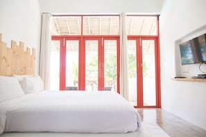 A bedroom with a large bed, a TV on the wall, and a sliding glass door leading to an outdoor area. - Pajamas Koh Chang (Ko Chang)